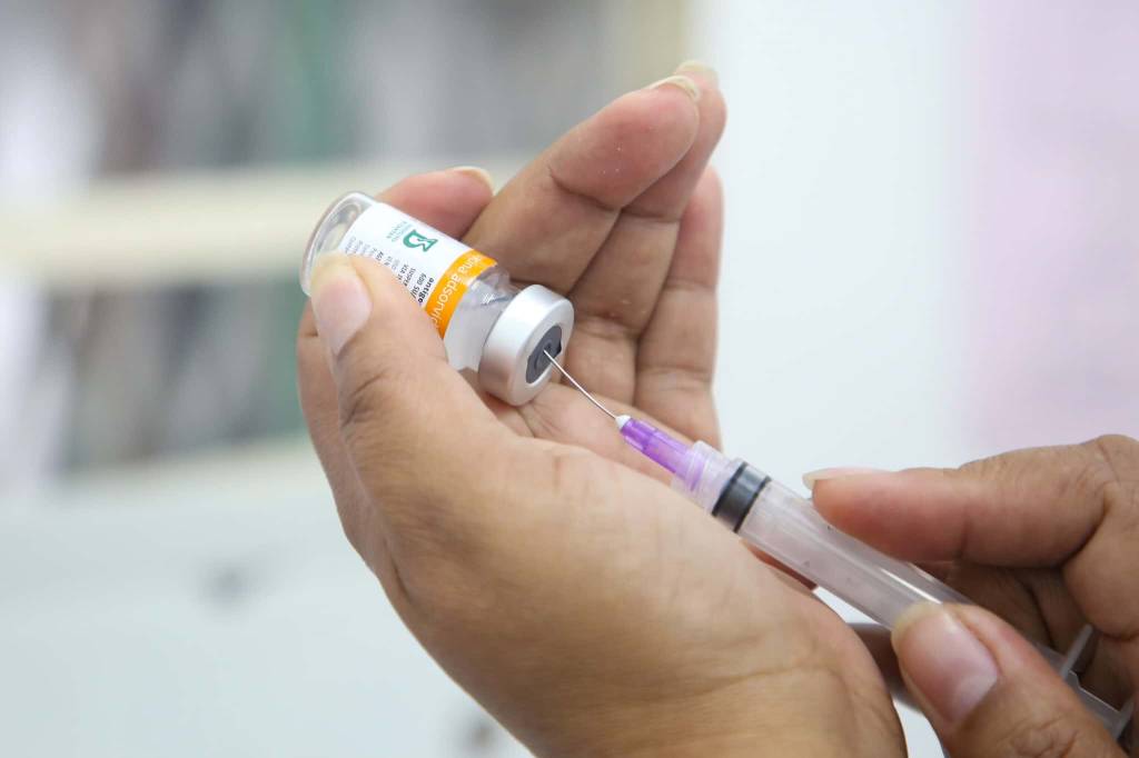 Imagem mostra enfermeira retirando dose de vacina de frasco com seringa