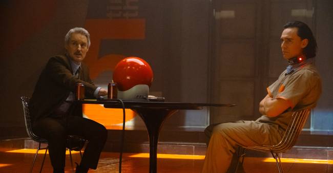 LOKI Sentados em uma mesa, Owen Wilson e Tom Hiddleston em cena de Loki