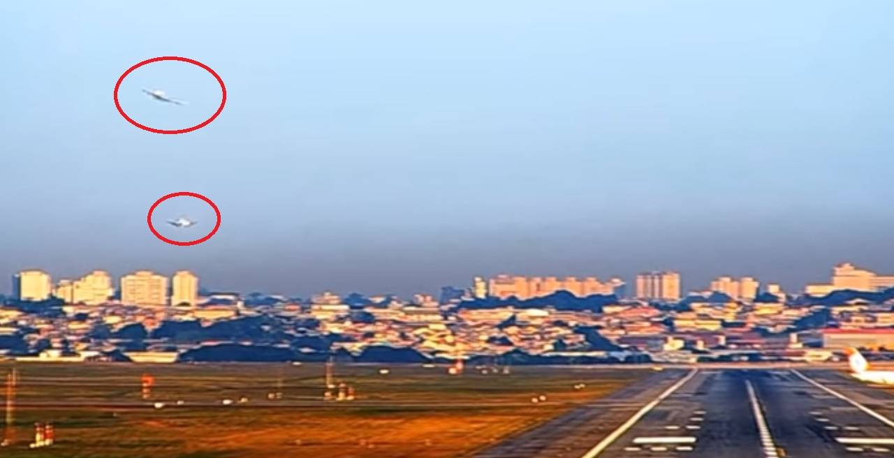A imagem mostra o aeroporto de Guarulho, visto do chão. É possível ver duas aeronaves, circuladas de vermelho, uma fazendo uma curva no céu e outra pousando na pista.