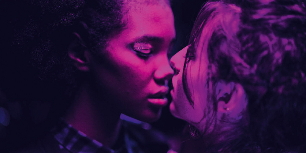 cena do filme boca a boca, em que duas mulheres estão quase se beijando sob uma luz roxa