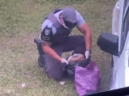 A imagem mostra um policial com um crânio, borrado, em mão. Ele está ajoelhado olhando para o objeto bem próximo ao chão