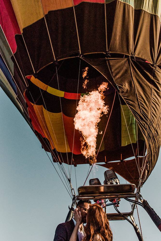 Foto mostra um balão nas alturas, com chamas para seu funcionamento. Nele, um casal se beija
