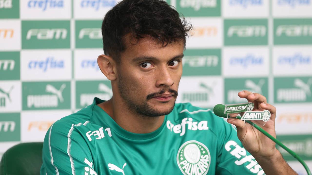 Gustavo Scarpa, meia do Palmeiras, segura microfone em coletiva e aparece com olhar desconfiado.