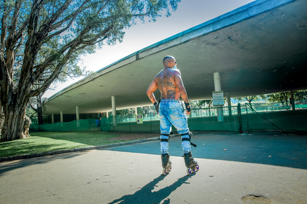 A imagem mostra Bruno, de patins, em frente a marquise fechada do Parque Ibirapuera