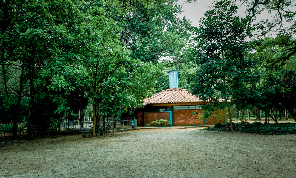 A imagem mostra uma pequena casa escondida entre árvores do parque