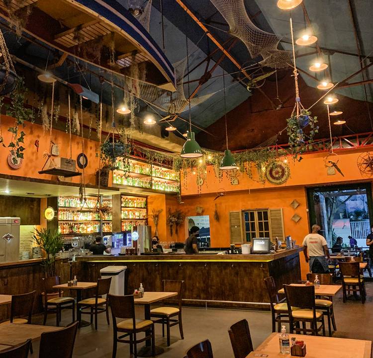Salão do bar Parô com mesas espaçadas e uma canoa pendurada no teto.
