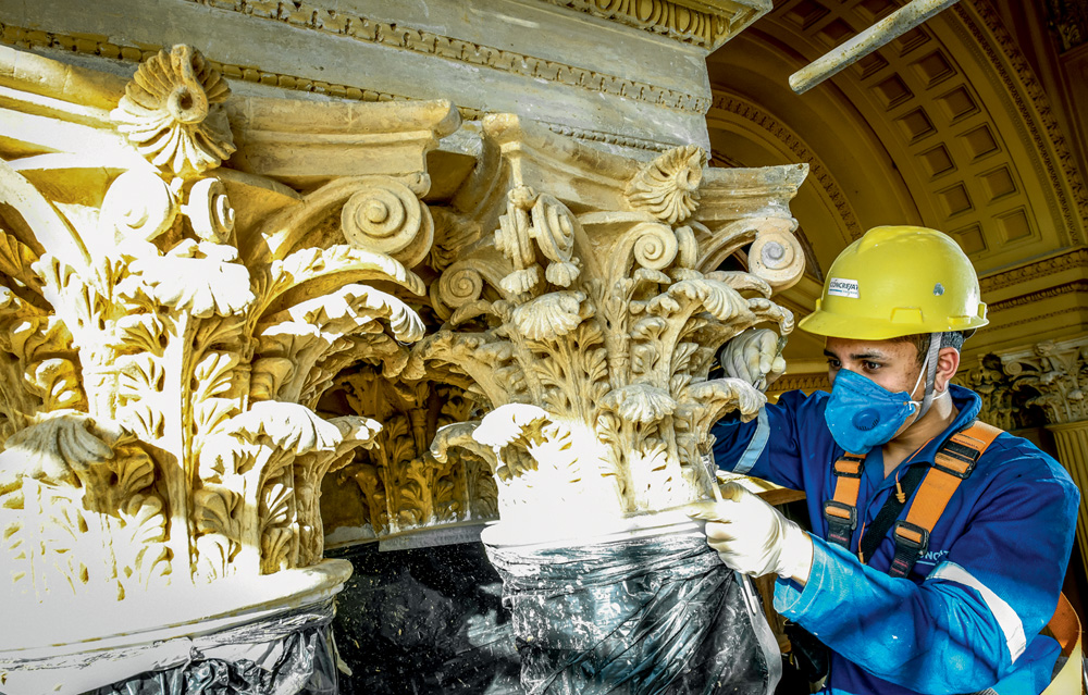 A imagem mostra Antonio, equipado com capacete e máscara, retocando uma estrutura com pincel.