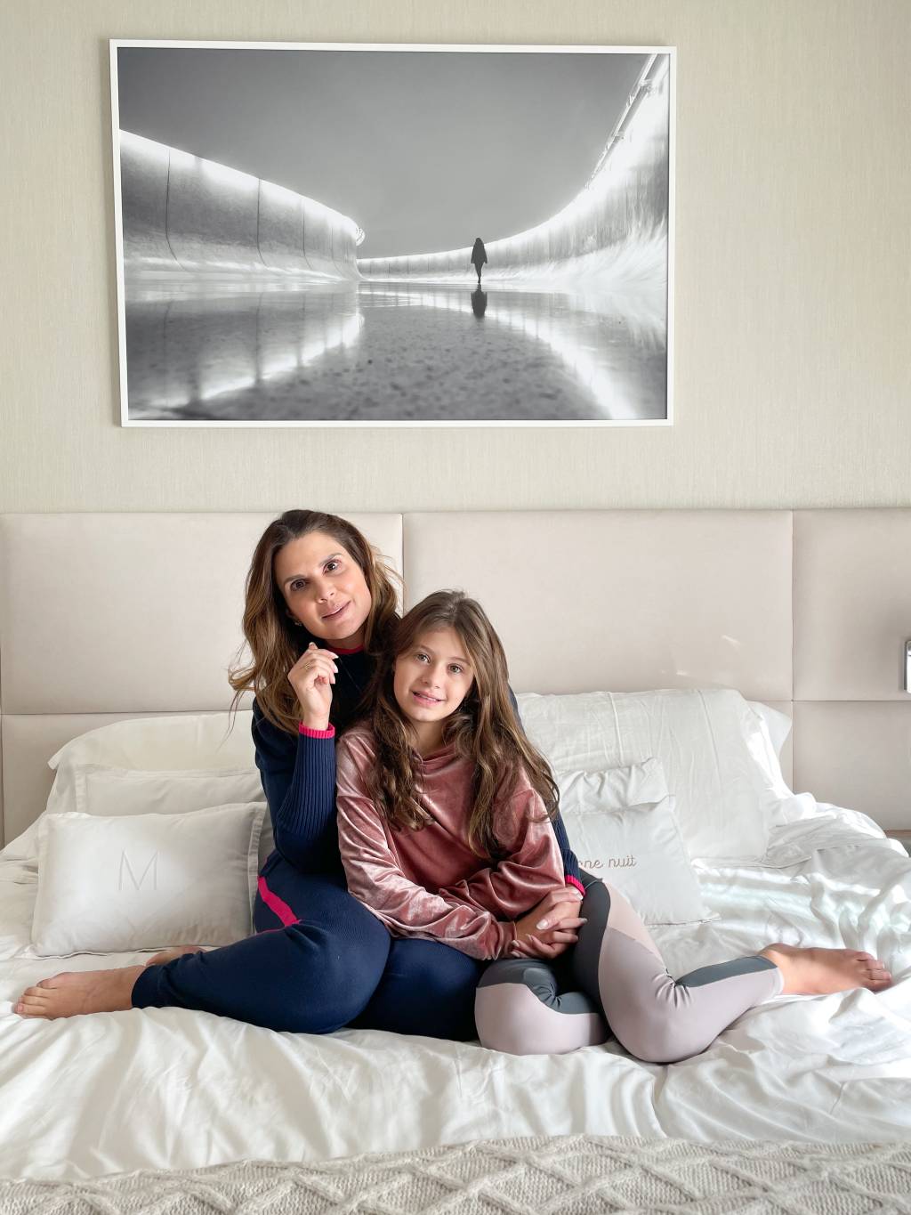 Mariana Kupfer e a filha Vicky posam sentadas na cama branca com fotografia produzida por Aryanne Valgas.