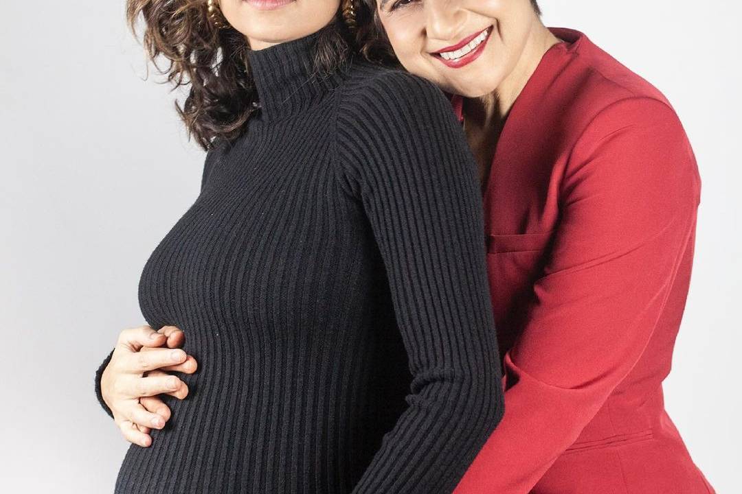 A imagem mostra Nanda Costa, com uma barriga de grávida de cinco meses, sendo abraçada por trás pela sua companheira, Lan Lanh, que sorri para a foto. Elas estão de lado e dá para ver nitidamente o relevo da barriga de Nanda.