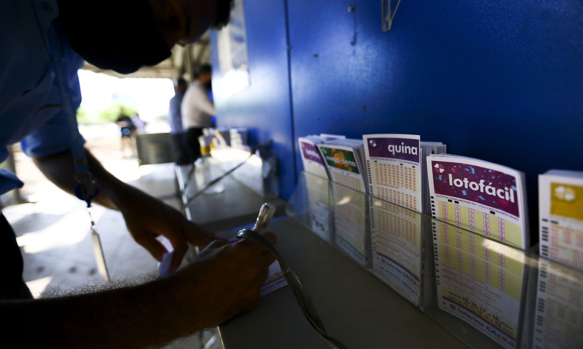 Apostadores fazem filas em casas lotéricas. Na foto, uma pessoa preenche números em papel da mega-sena.