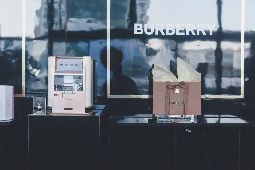 Foto mostra estande da marca Burberry com uma embalagem e uma máquina de customizar pingentes