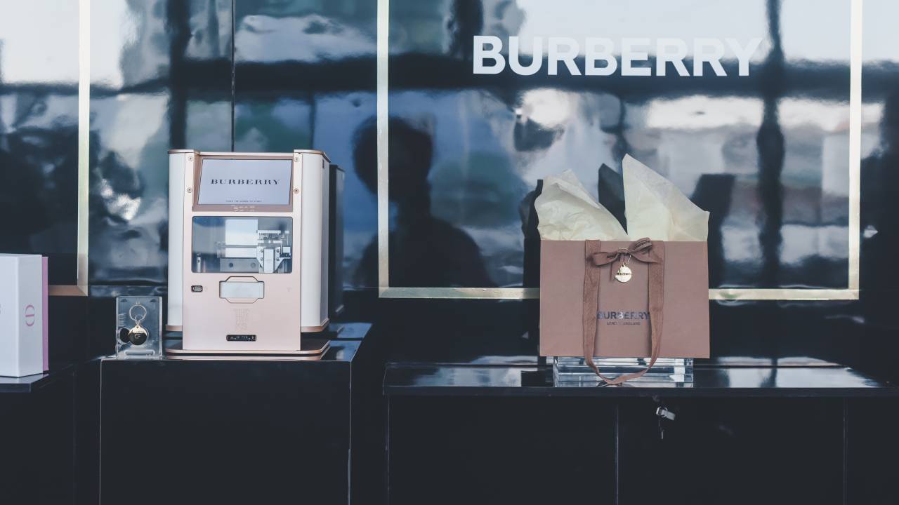 Foto mostra estande da marca Burberry com uma embalagem e uma máquina de customizar pingentes