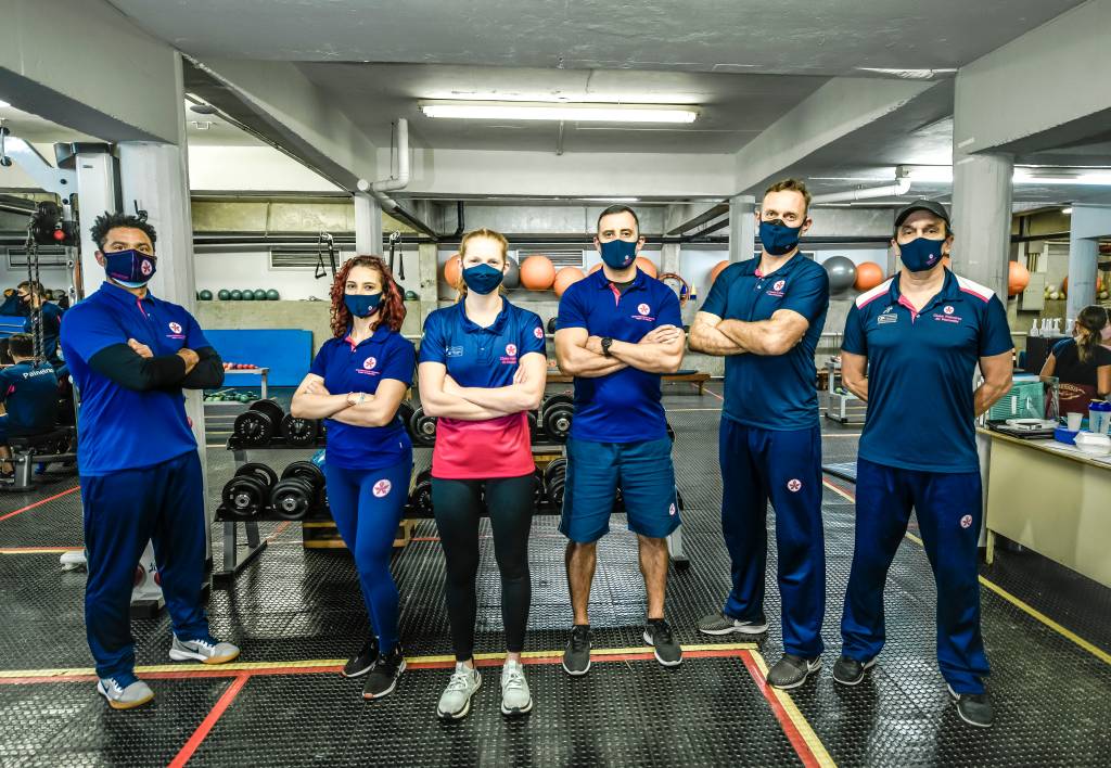 A imagem mostra Stephanie e outras pessoas com uniforme do Paineiras em uma academia, todos de máscara e braços cruzados
