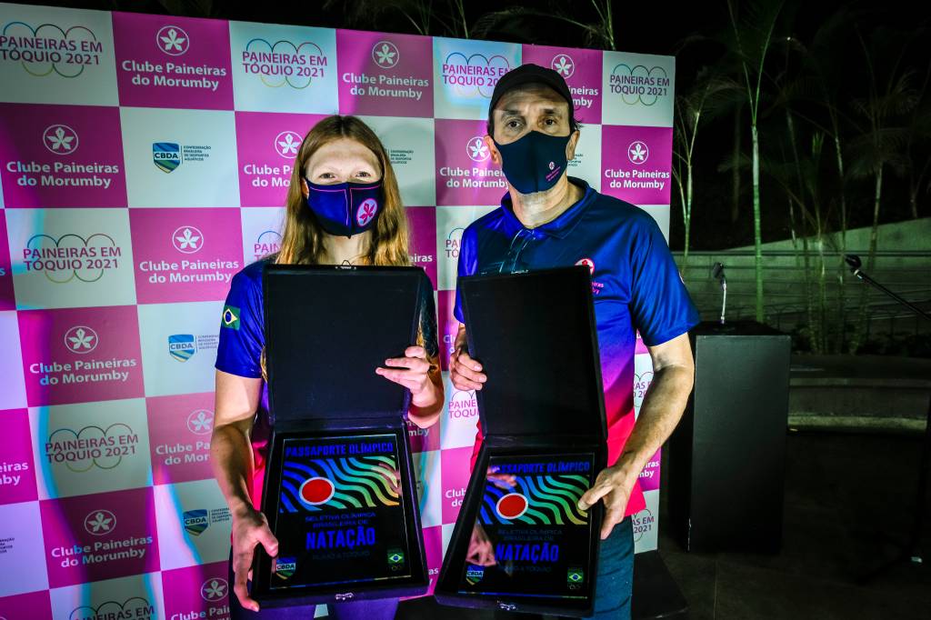A imagem mostra Stephanie e Wlad, ambos segurando placas olímpicas e mostrando elas para a câmera