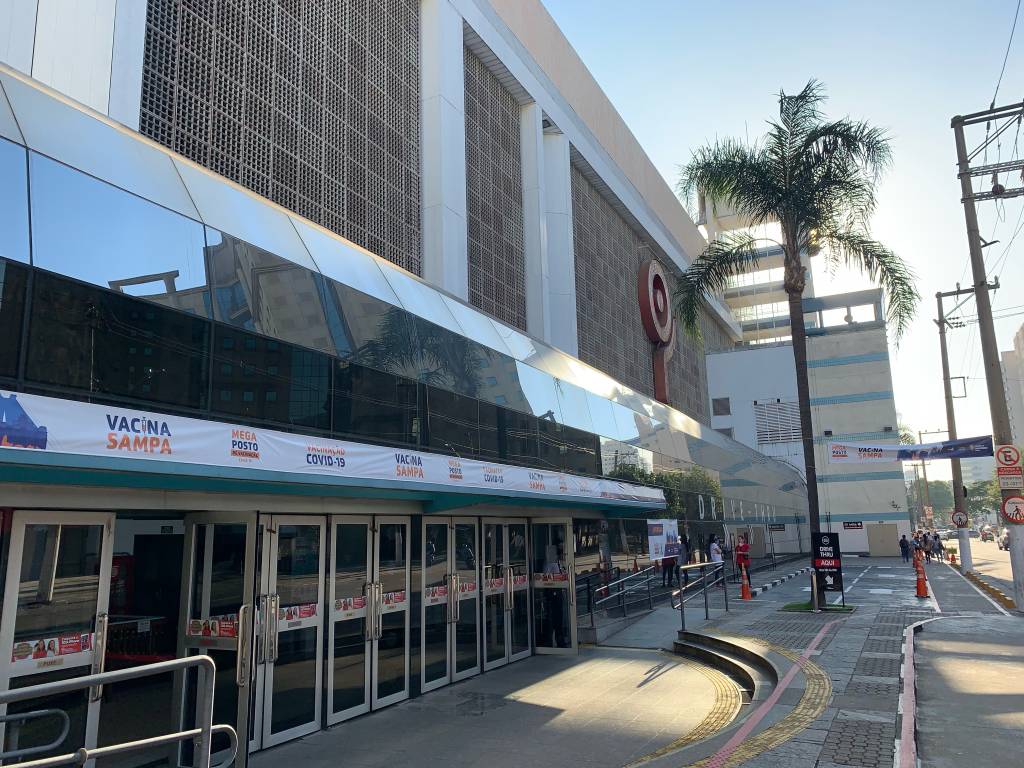 A imagem mostra a fachada do Shopping Ibirapuera com um banner discreto escrito "Vacina Sampa"