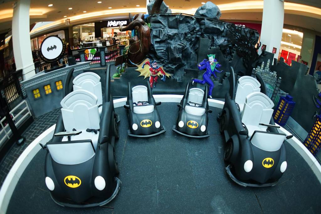Carrinhos elétricos pretos com o símbolo do batman estão estacionados em um cenário do filme do personagem no shopping Mooca Plaza