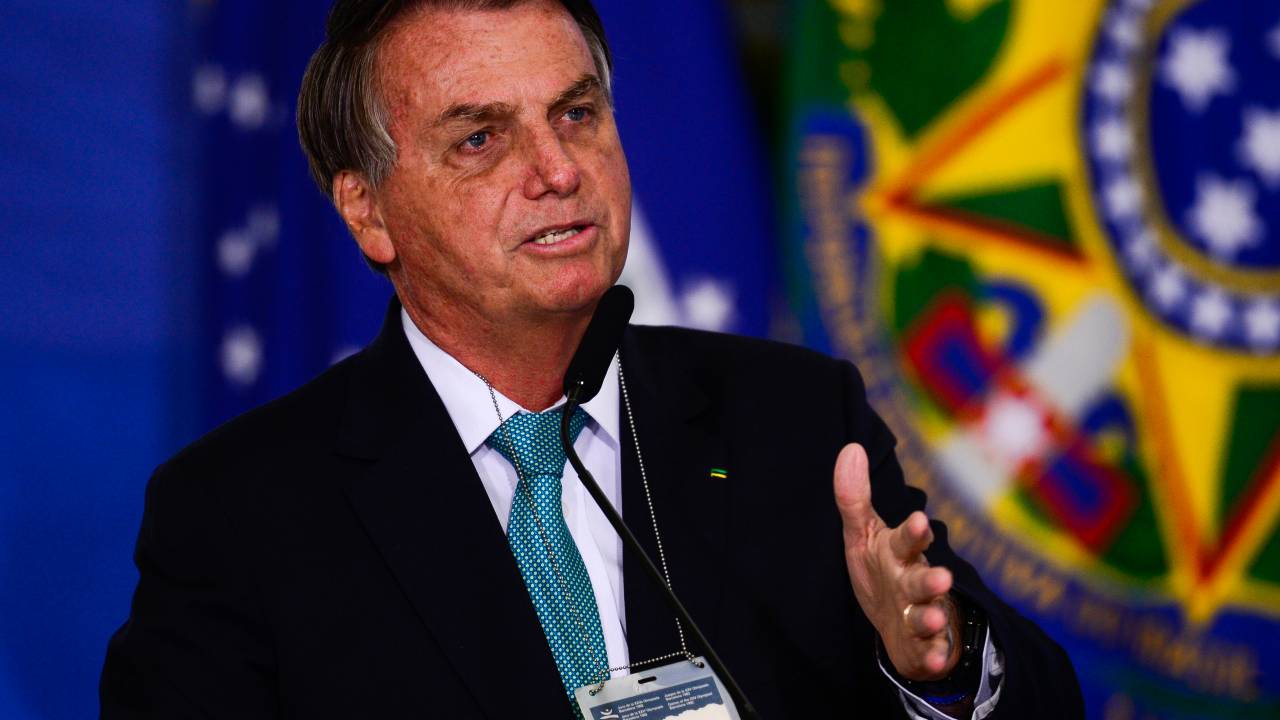 Jair Bolsonaro aparece durante cerimônia, usando terno e gravata, discursando diante de microfone