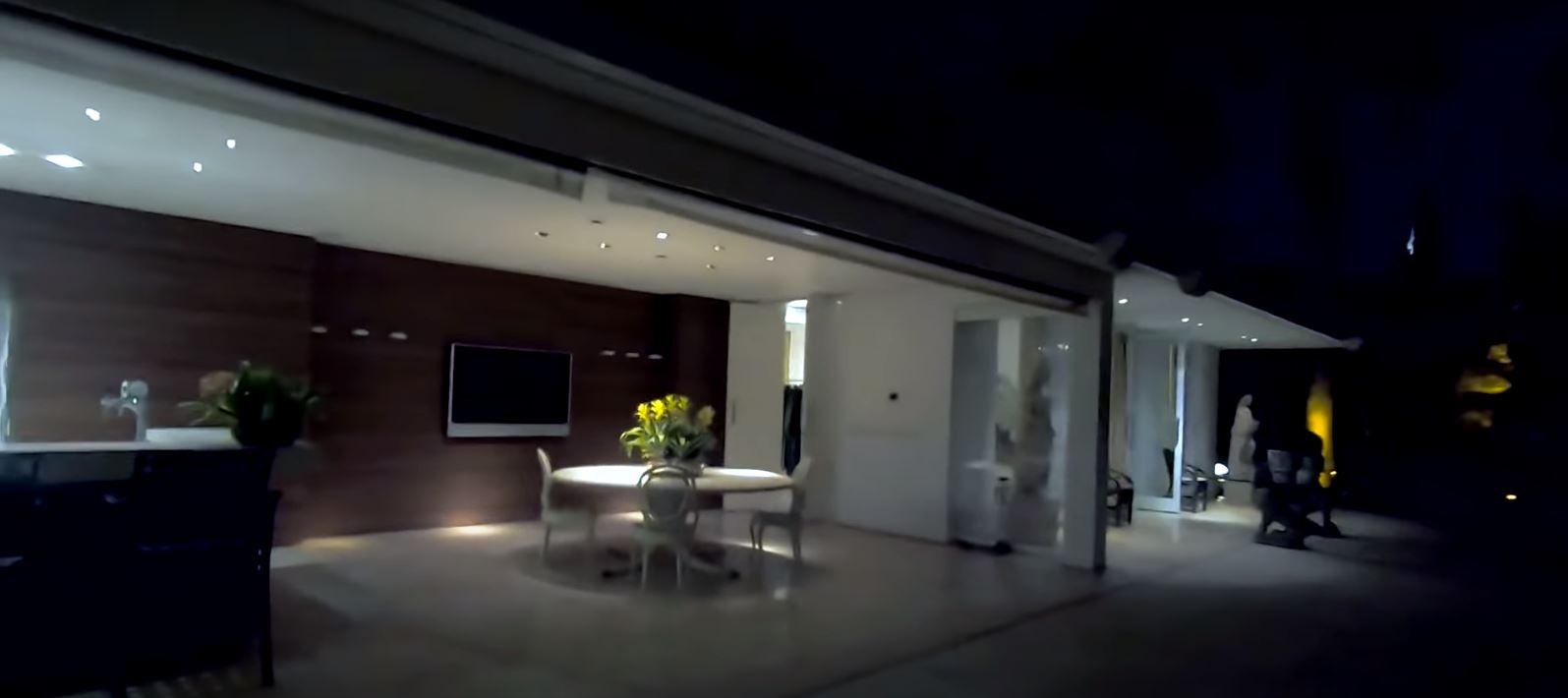 área externa da casa, com abertura entre os ambientes interno e externo e uma televisão e mesa redonda na parte coberta