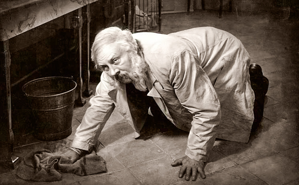 La foto mostra il porta-pellicola inginocchiato sul pavimento, che lo pulisce con uno straccio mentre alza lo sguardo con disapprovazione.