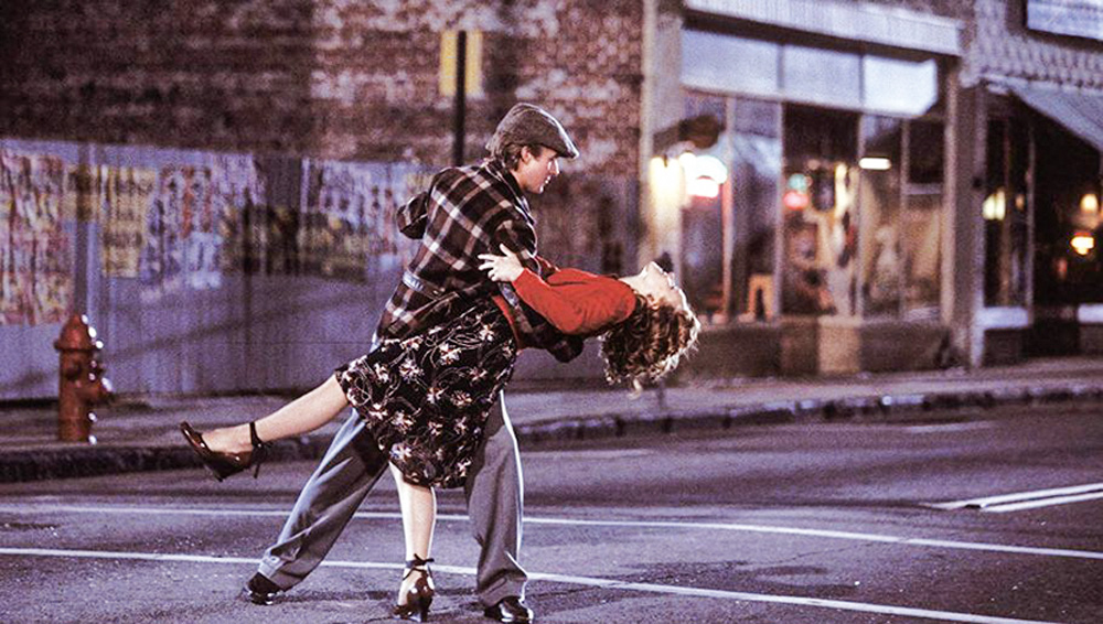 A imagem mostra Ryan Gosling e Rachel McAdams dançando na rua, com ele segurando ela com o braço direito enquanto ela faz o movimento de cair para trás.