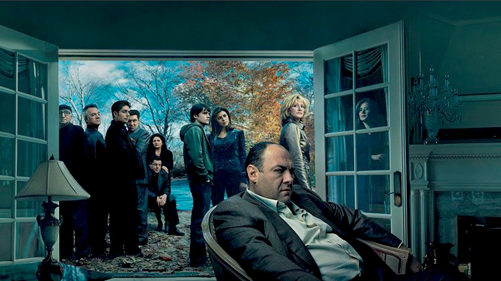 A imagem mostra os protagonistas de Os Sopranos em uma sala de uma casa. Todos com expressões sérias.