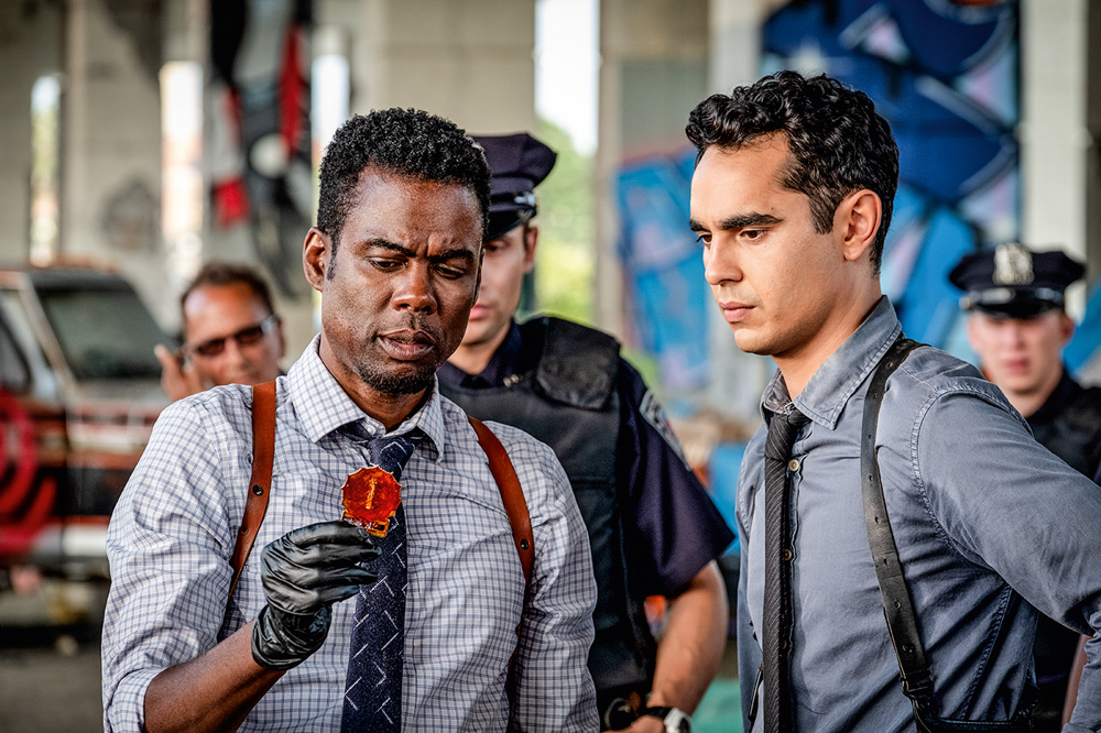 A imagem mostra a dupla de atores com as roupas de policiais analisando um objetivo nas mãos de Chris.