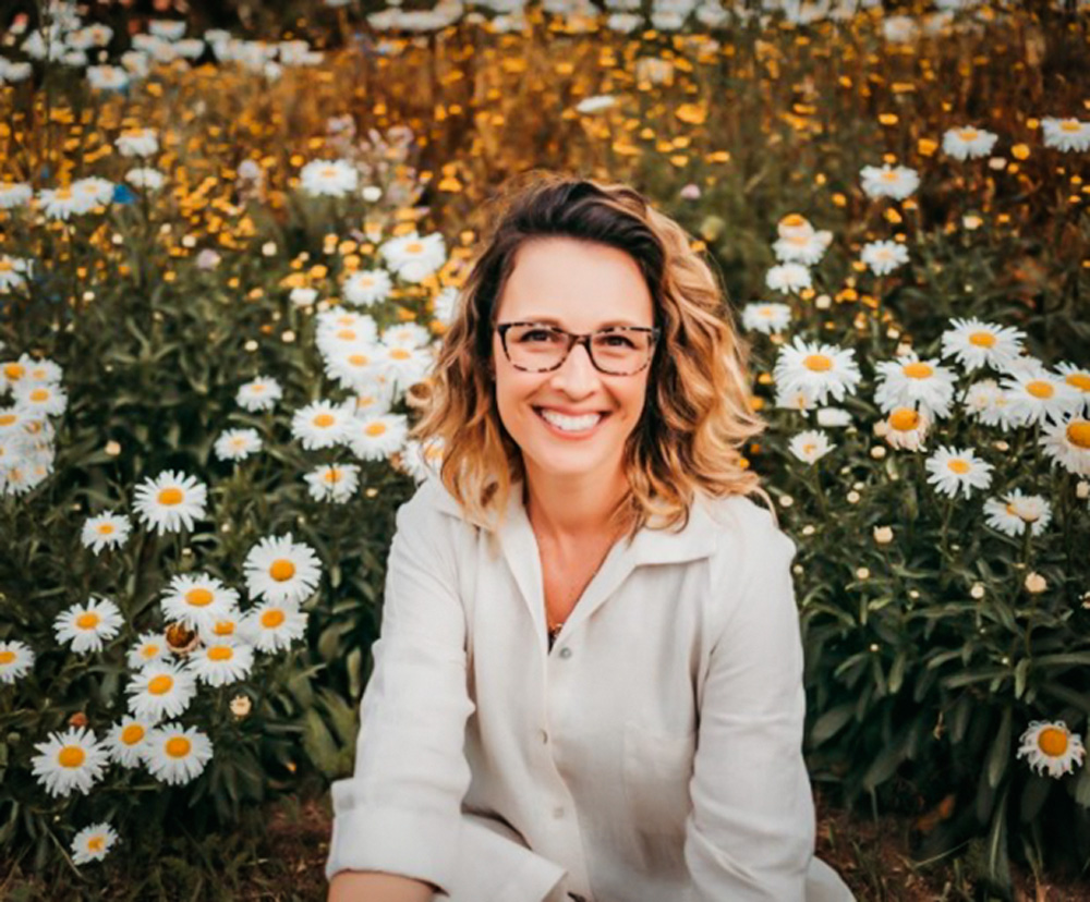 regina sorrindo para a foto com flores ao fundo