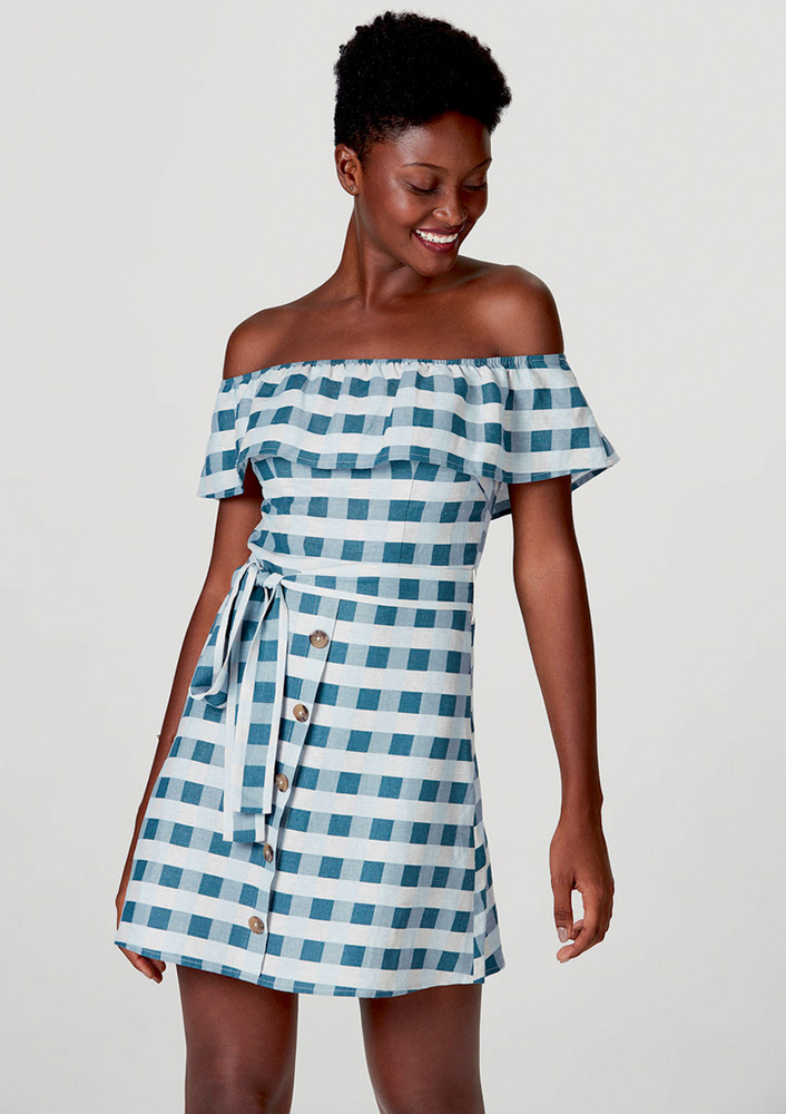 vestido.jpg Mulher negra sorri e olha pra baixo vestida com vestido azul e branco xadrez