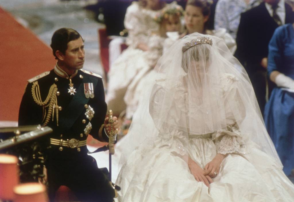 Príncipe Charles e sua esposa, a Princesa Diana, no altar da Catedral. charles segura uma espada apoiada em sua outra ponta no chão e diana está com o véu sobre sua face