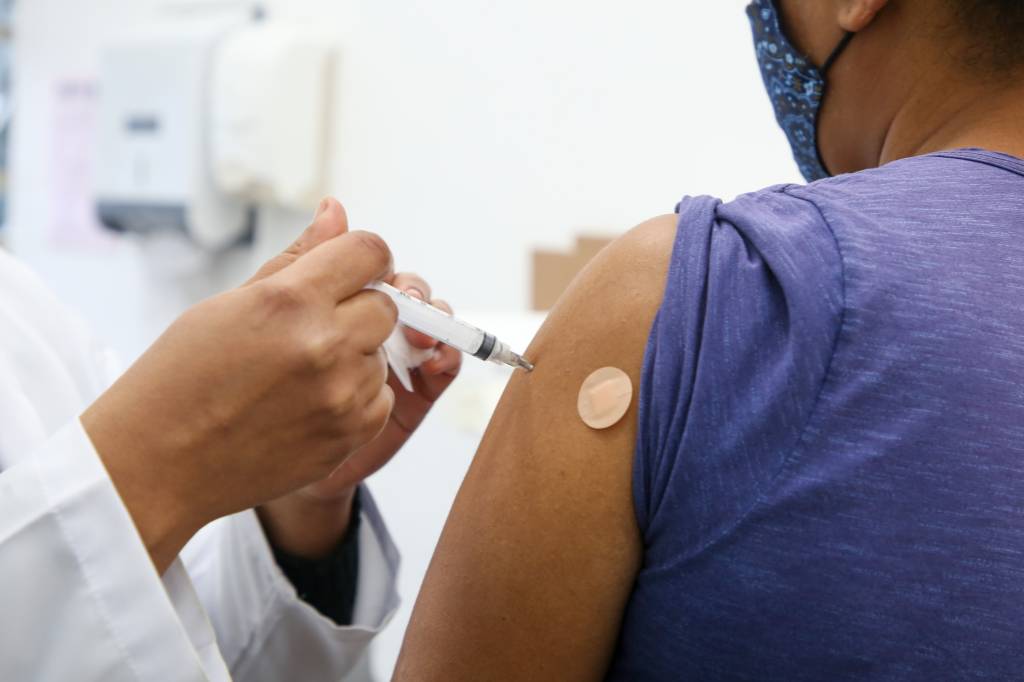 Imagem mostra enfermeira aplicando dose de vacina no braço de mulher