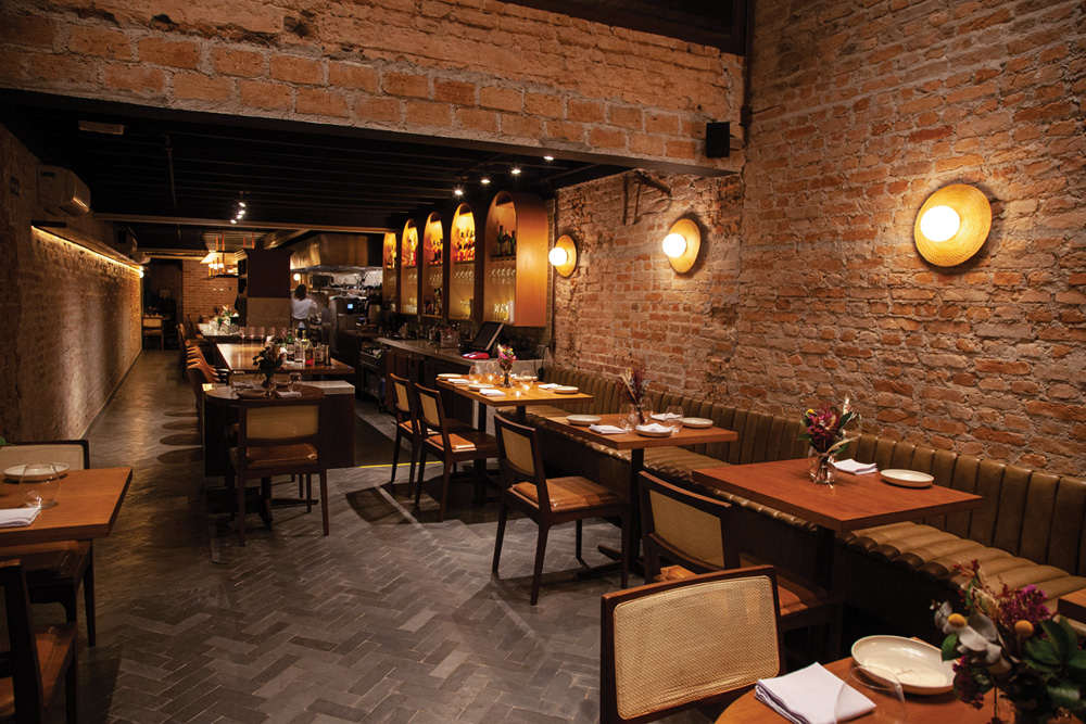 Salão do restaurante Nelita, com paredes de tijolo aparente e mesas alinhados do lado direito.