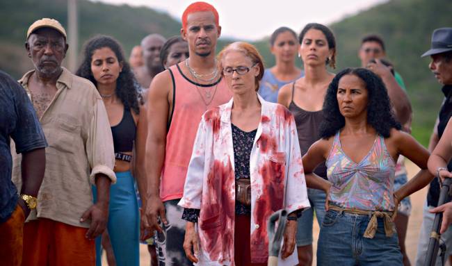 A imagem mostra uma cena de Bacurau, com Sonia Braga e Silvero Pereira em frente à várias pessoas. Elas duas estão com expressões sérias.