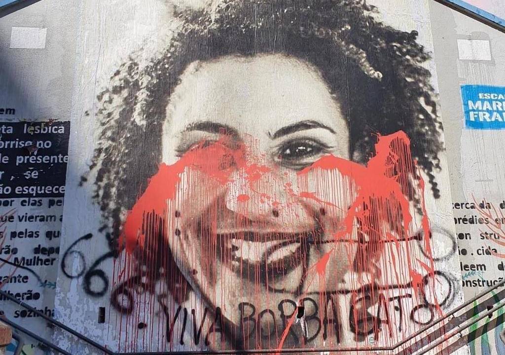 A imagem mostra o painel com o rosto de Marielle Franco coberto por tinta vermelha e a inscrição Viva Borba Gato