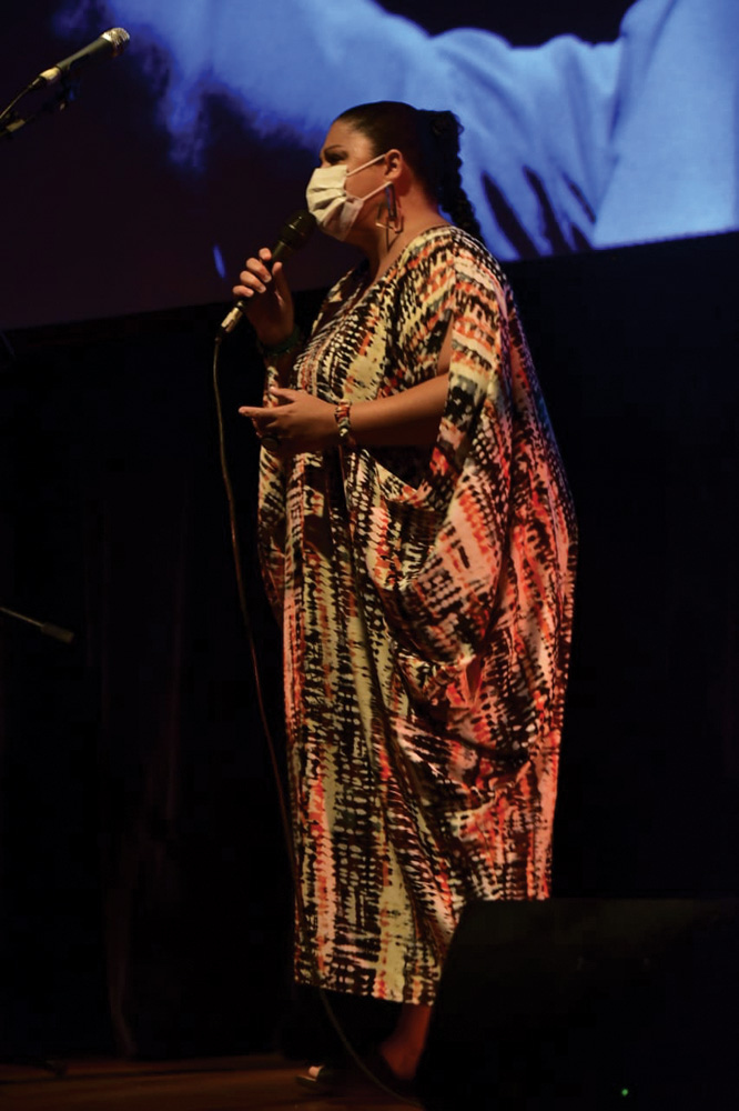 De vestido e máscara, uma mulher canta em um palco de teatro