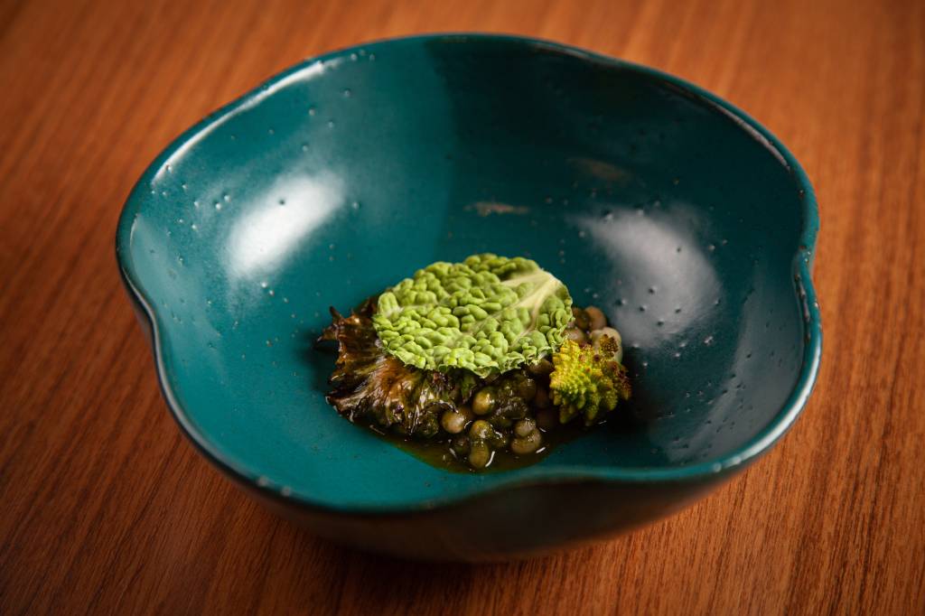 Refogado de feijão-manteiguinha com folhas verdes servido em uma cumbuca de cerâmica de cor azul sobre bancada de madeira.