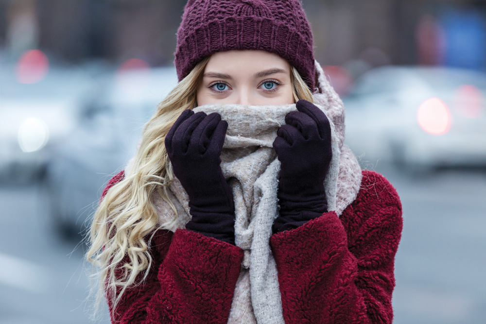 Mulher jovem sentindo frio no inverno. Ela coloca um cachecol em frente à boca e o nariz