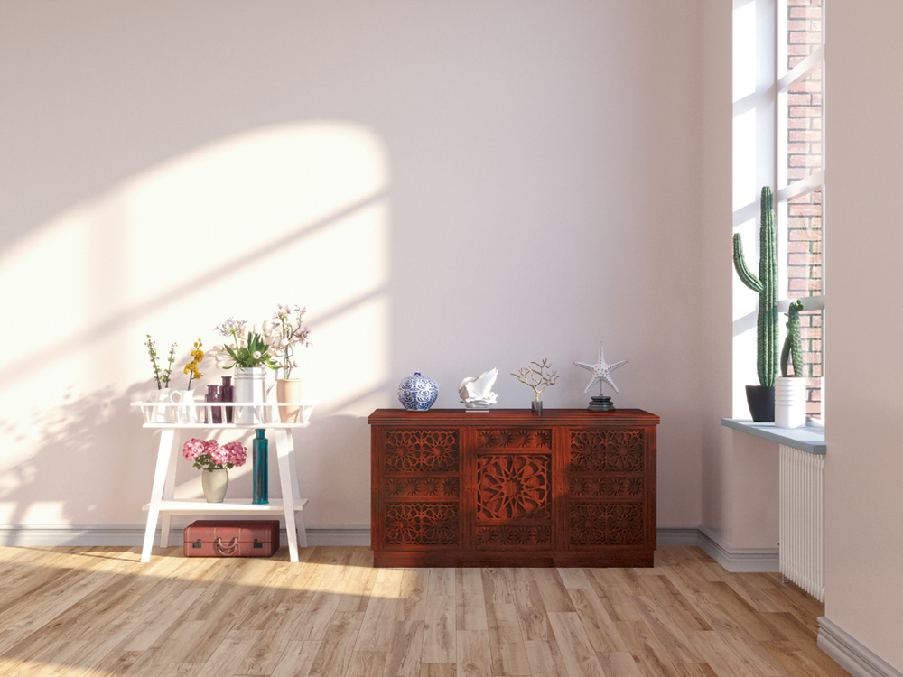 Vista para um cômodo de madeira, uma mini estante com flores e, ao lado, uma janela com bastante luz do sol entrando