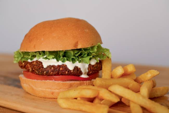 Hamburguinho Hambúrguer de faláfel do Hamburguinho ao lado de fritas palito sobre mesa de madeira.