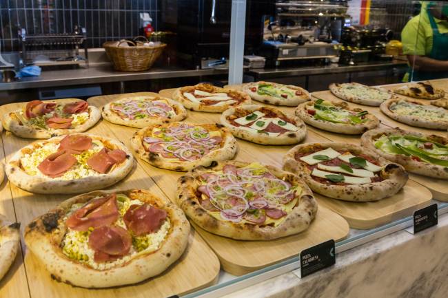 Pizzas individuais em vitrine sobre assadeiras de madeira.