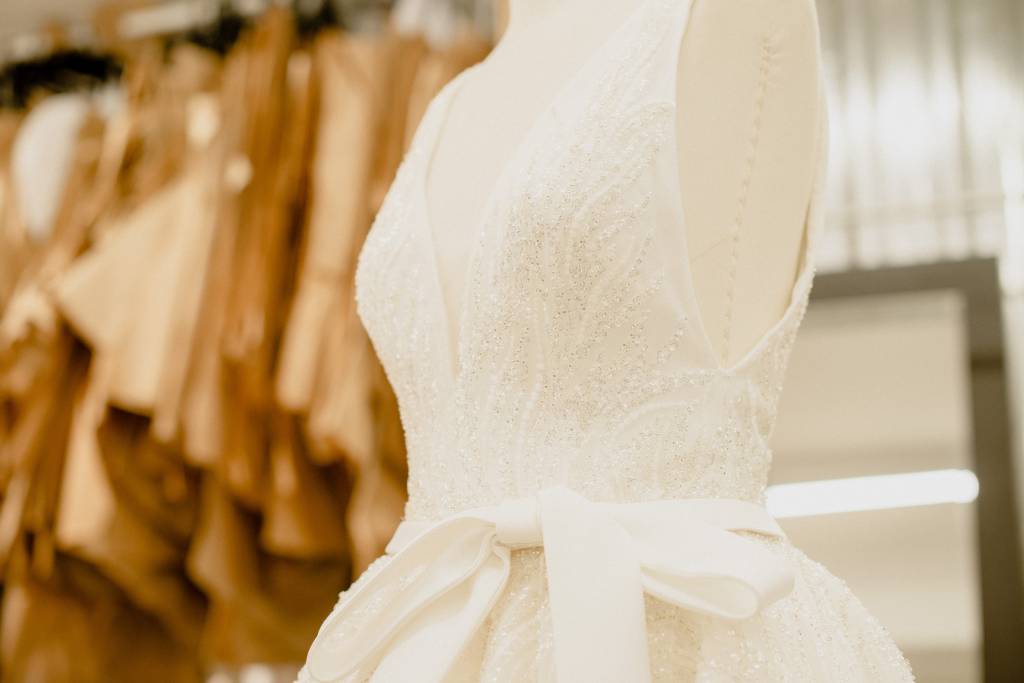 Imagem exibe parte de vestido de noiva branco com laço na altura da cintura.
