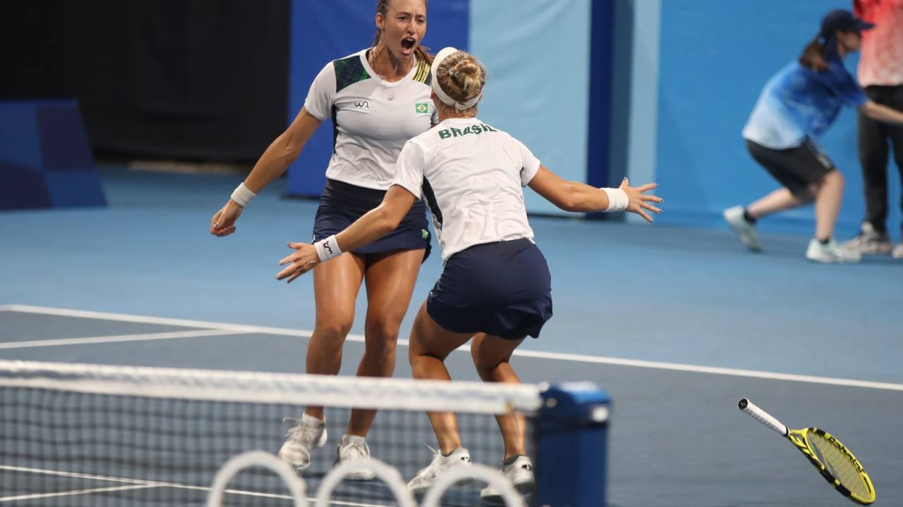 A imagem mostra Luisa Stefani e Laura Pigossi, na quadra de tênis, comemorando uma para outra, quase se abraçando.