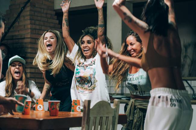 Participantes do reality show Casa Malibu pulando e gritando em volta de mesa.