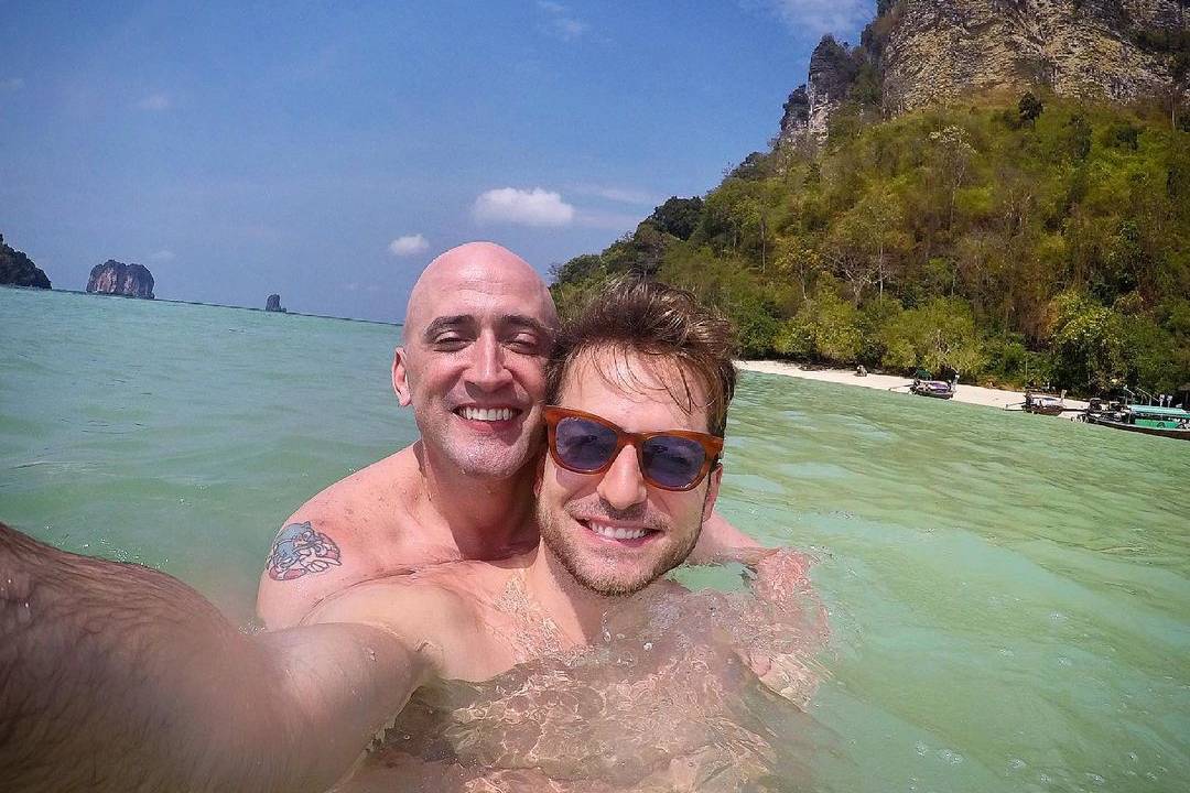 A imagem mostra Thales, com um celular, tirando uma selfie sua com Paulo Gustavo dentro do mar