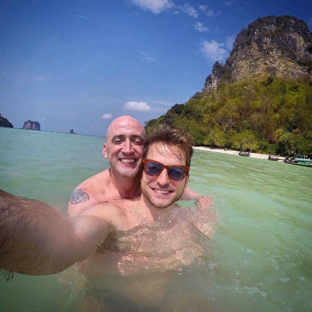 A imagem mostra Thales, com um celular, tirando uma selfie sua com Paulo Gustavo dentro do mar