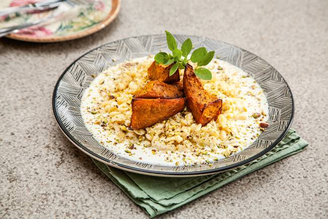 Spätzle coberto por três pedaços de abóbora-cabotiá assada e ramo de manjericão.