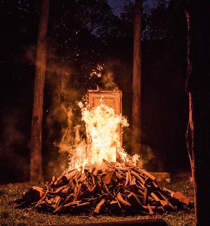 porta em uma floresta envolta em uma pilha de toras queimando