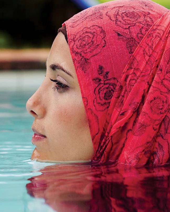 Imagem mostra rosto de perfil de mulher utilizando o véu do hijab saindo da piscina