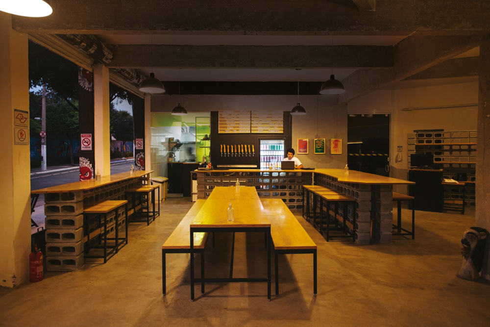 Salão da Cervejaria Central na Barra Funda, em meia luz com mesas e bancos longos de madeira ao centro, direita e esquerda.