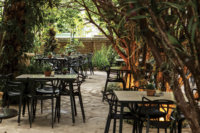 Mesas ao ar livre em meio a árvores no jardim do restaurante Ama.zo.