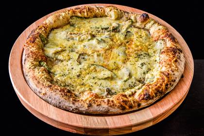 Dia da Pizza - Bráz Pizza de abobrinha com queijos em travessa de madeira com fundo preto.